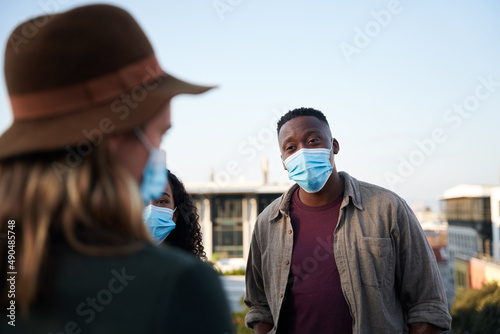 Black male and multi-cultural friends chatting on a rooftop terrace with masks on. City living and good times.