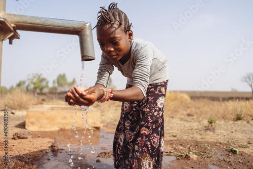 Valokuva Pretty little black girl hunched over by a West African village pump, happily ho