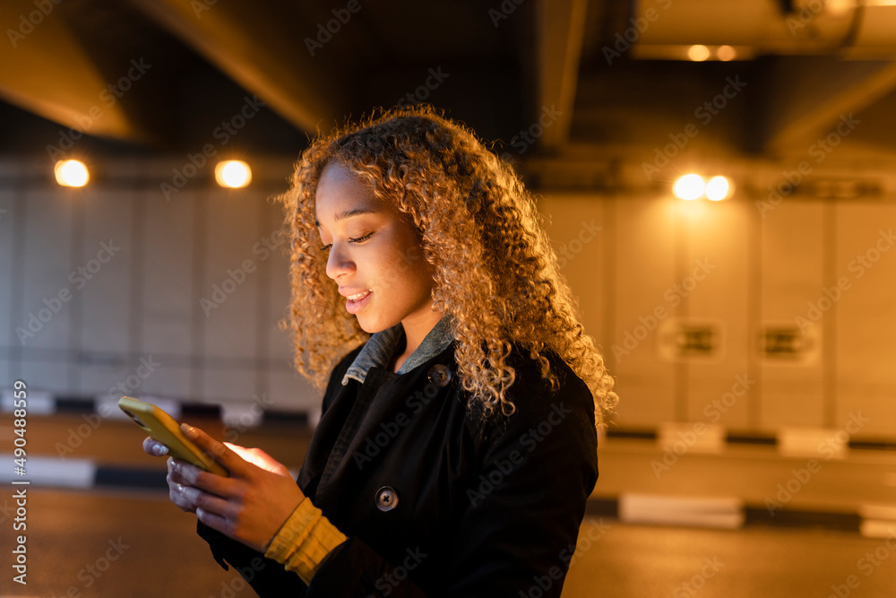 pretty woman with curly blonde hair, at night, in the city, looking at her mobile phone