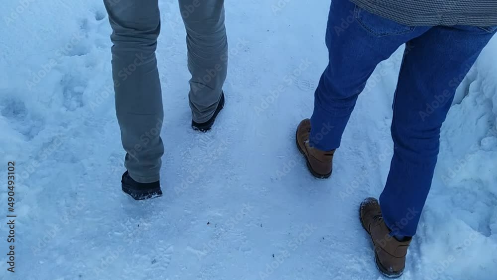 feet of a couple of young people walking on a snowy road at daytime feet of a couple of young people walking on a snowy road at daytime