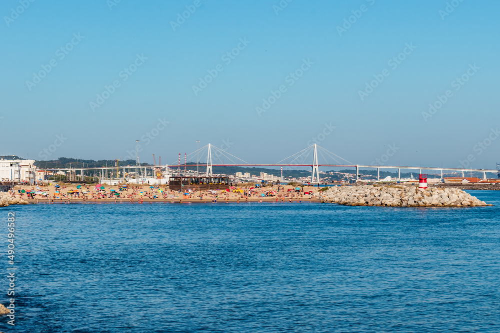 Breakwater with a small sandy beach in with silhouettes of holidaymakers and a bridge in the background, Figueira da Foz PORTUGAL Breakwater with a small sandy beach in with silhouettes of holidaymakers and a bridge in the background, Figueira da Foz PORTUGAL