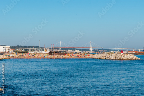 Breakwater with a small sandy beach in with silhouettes of holidaymakers and a bridge in the background, Figueira da Foz PORTUGAL