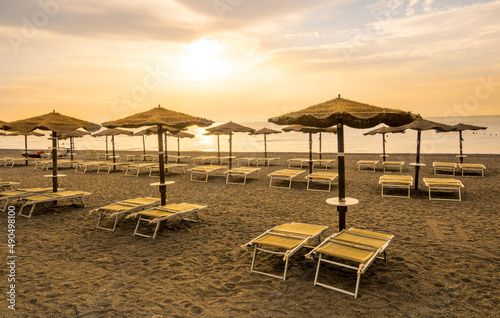  empty beach during beautiful sunrise or sunset with chaise loungues and nice umbrellas with blue sea  sun glow and amazing cloudy sky on thr background