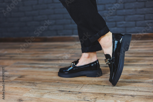 Close-up female legs in black trousers and leather black shoes. Women's shoes in patent leather with a metal buckle. New spring-summer collection of women's leather shoes 2022
