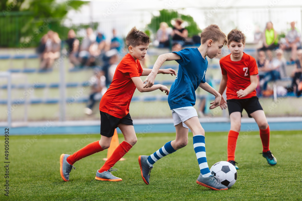 Young boys playing a football game. Training and soccer match between youth  school teams. Junior competition between players running and kicking a soccer  ball. Game of football tournament for kids. Stock-Foto