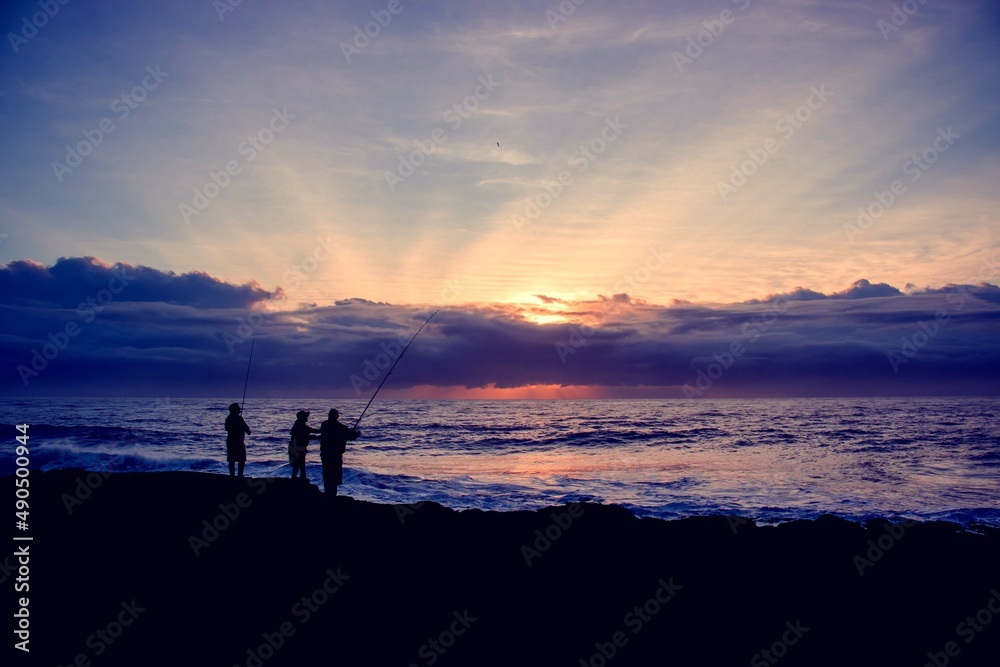 Men standing on the edge of rocks to catch fish from the ocean