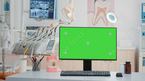 Monitor with green screen on desk in empty dentist office. Nobody in stomatological cabinet with oral care equipment and chroma key for mockup template and isolated background.