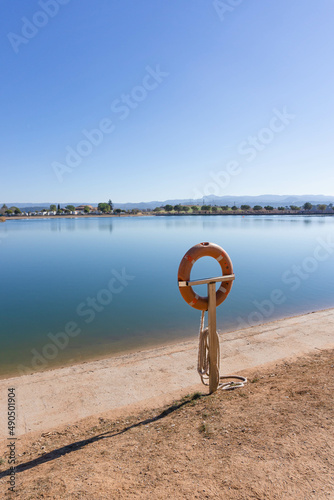 A pole with a lifesaver float in front of a lake