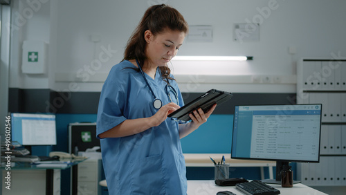 Woman working as nurse and holding digital tablet for checkup visit in cabinet. Medical assistant using technology and modern device for healthcare appointment and healing treatment.