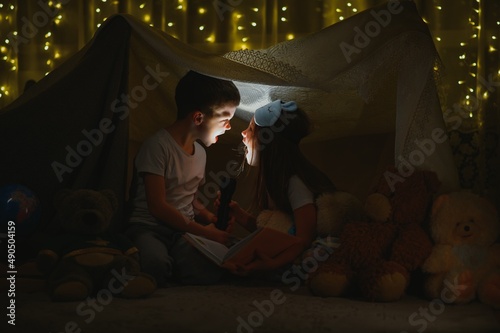 Two little child play at home in the evening to build a camping tent to read books with a flashlight and sleep inside. Concept of: game, magic, creativity, alarm systems © Serhii