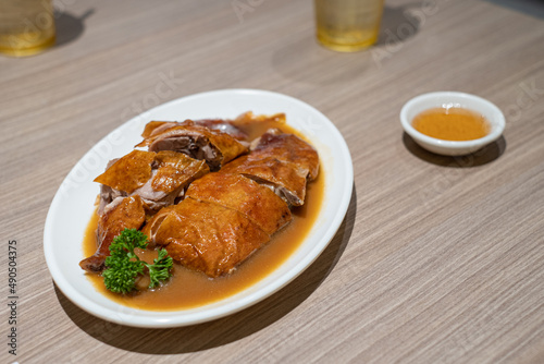 Roasted duck on white plate topped with black gravy herbal sauce on wooden Table. Hongkong cuisine, Chinese cuisine