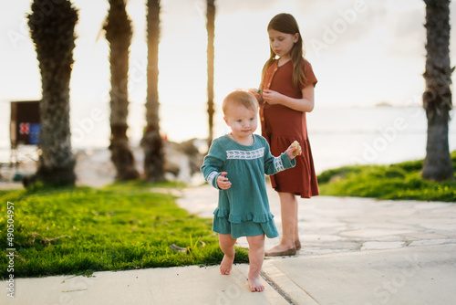 Cute European kid girl in dress on sea. Girl with her sister at sunset on ocean. Walks along seashore in silence at sunset. Kids run stone path near sea, happy childhood and sibling relationships © natalialeb