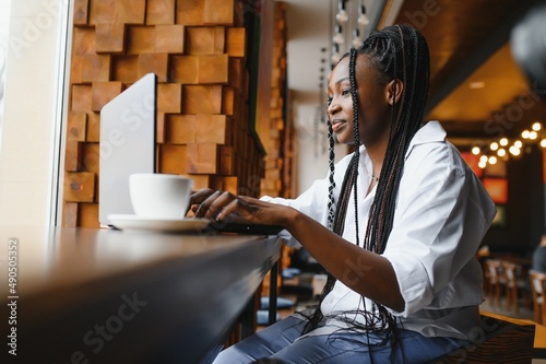 Side view of black lady enjoying morning coffee and checking emails on laptop, cafe interior, empty space
