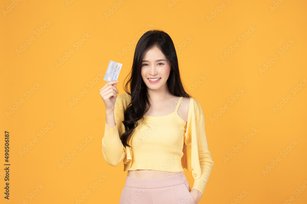 Cheerful young asian woman in yellow T-shirt holding bank card isolated on yellow background Cheerful young asian woman in yellow T-shirt holding bank card isolated on yellow background