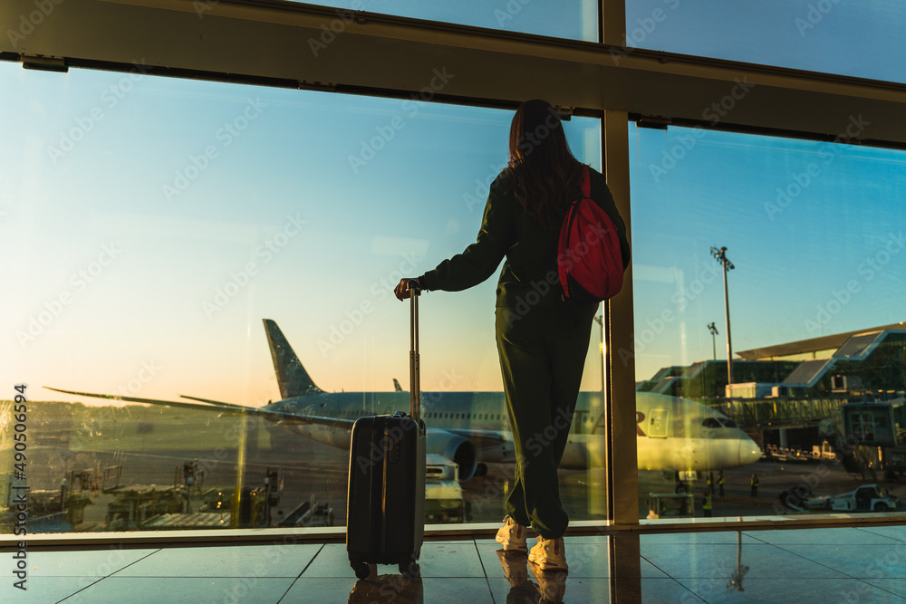 woman with carry-on suitcase looking through the windows of the airport.