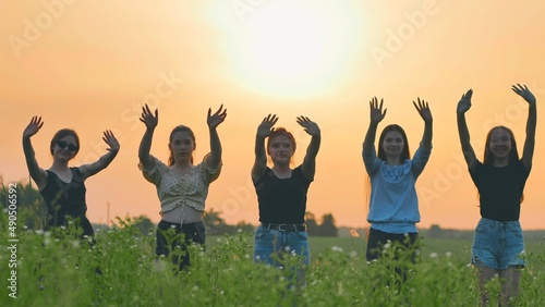 Girls friends waving their hands to the setting sun on the background of the sunset.
