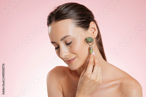 Pleasant woman using jade roller for massaging face