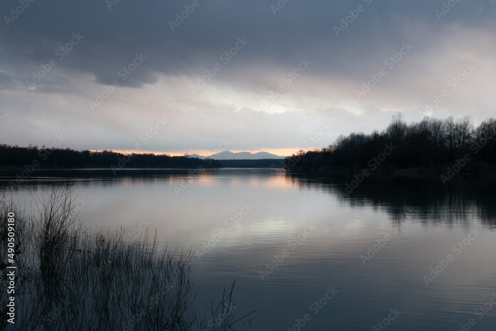 Landscape of river and mountain during overcast evening - forest and reed silhouette