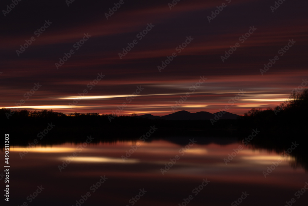 Rural landscape at twilight with fading light in long exposure - abstract dark cloud over mountain silhouette and reflection in river water