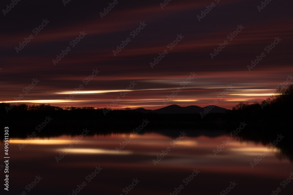 Rural landscape at twilight with fading light in long exposure - abstract dark cloud over mountain silhouette and reflection in river water Rural landscape at twilight with fading light in long exposure - abstract dark cloud over mountain silhouette and reflection in river water