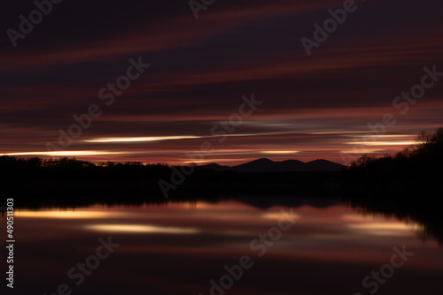 Rural landscape at twilight with fading light in long exposure - abstract dark cloud over mountain silhouette and reflection in river water