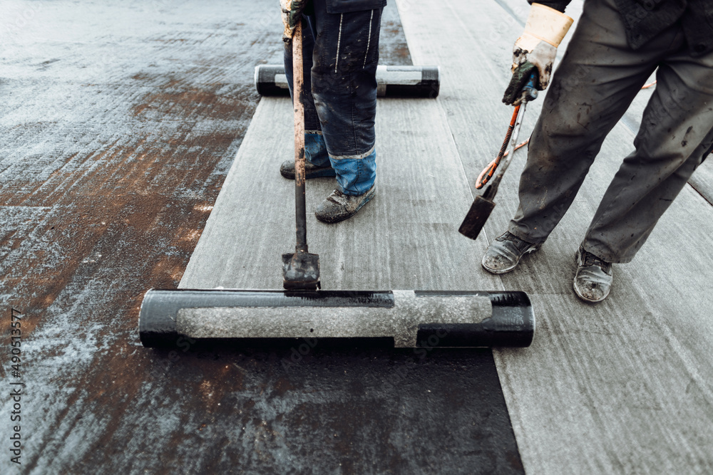 Foto de Construction workers, roofers installing rolls of bituminous