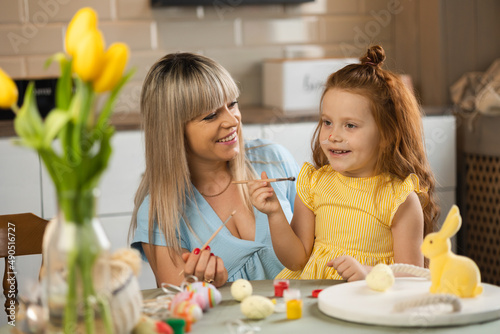 Cheerful mother and daughter coloring eggs for Easter holidays