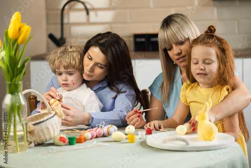 Two mothers with their children paint Easter eggs in the kitchen
