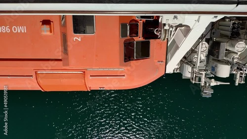 Big safety boat hanging from the side of a cruiser seen from above. Someone from maintenance is inside and opens the different windows on the boat top to carry a routine check. photo