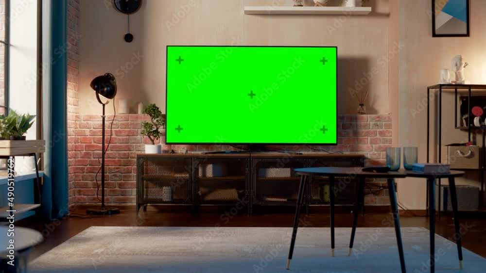Stylish Loft Apartment Interior with TV Set with Green Screen Mock Up Display Standing on Television Stand. Empty Living Room at Home with Chroma Key Placeholder on Monitor. Zoom In Shot.
