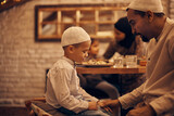 Muslim father holds son's hand while talking to him during dinner in dining room.