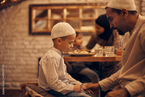 Muslim father holds son s hand while talking to him during dinner in dining room.