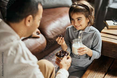 Happy Muslim girl eats date while talking to her father at home.