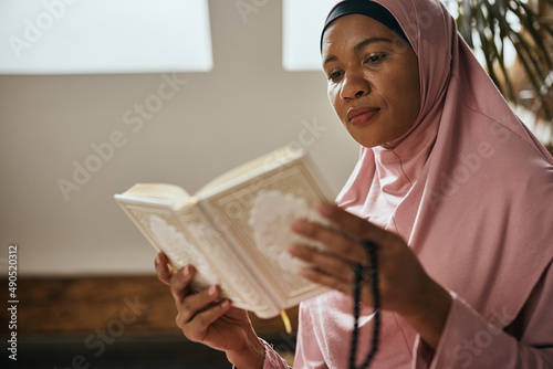 Valokuvatapetti Black Muslim woman reads the holy book Quran at home.