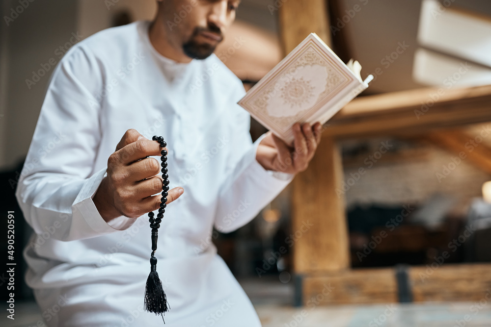 Close-up of Muslim man prays while reading Koran and holding misbaha beads.