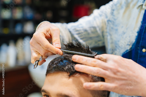 hairdresser makes a haircut for a brunet man with a scissors in a barbershop