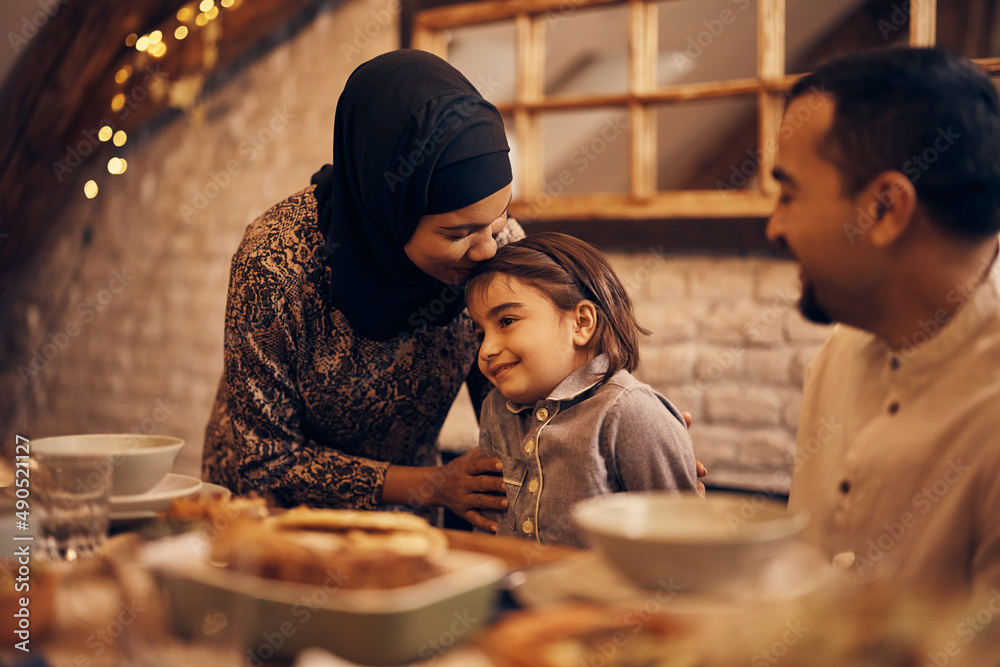 Loving Muslim mother kisses her daughter during family meal at dining table. Loving Muslim mother kisses her daughter during family meal at dining table.