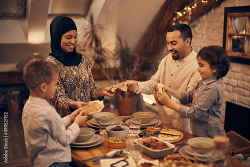 Happy Middle Eastern family shares pita bread at dining table on Ramadan.