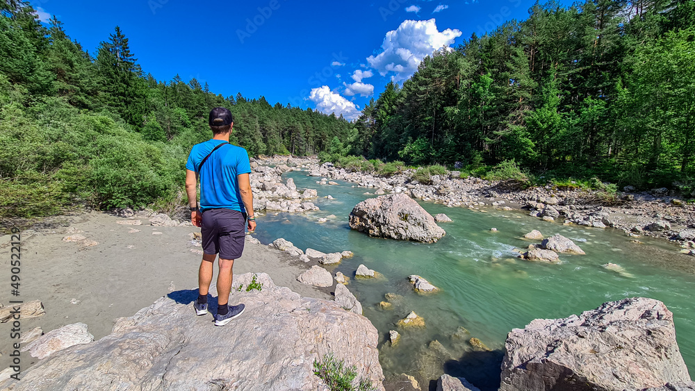 Man standing on rock with scenic view on river Gail flowing through the Schuett in natural park Dobratsch in Villach, Carinthia, Austria. Gailtaler and Villacher Alps. Crystal clear water. Freedom