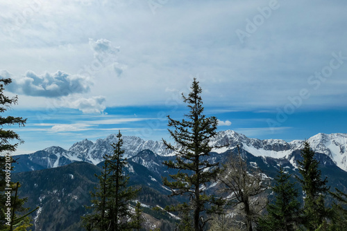 Scenic view of snow capped mountain peaks of Karawanks near Sinacher Gupf in Carinthia, Austria. Mount Wertatscha and Hochstuhl (Stol) is visible through dense forest in early spring. Sunny Rosental photo