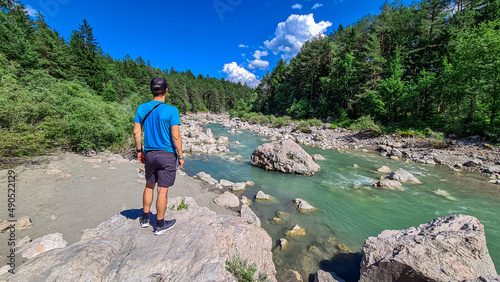 Man standing on rock with scenic view on river Gail flowing through the Schuett in natural park Dobratsch in Villach, Carinthia, Austria. Gailtaler and Villacher Alps. Crystal clear water. Freedom photo