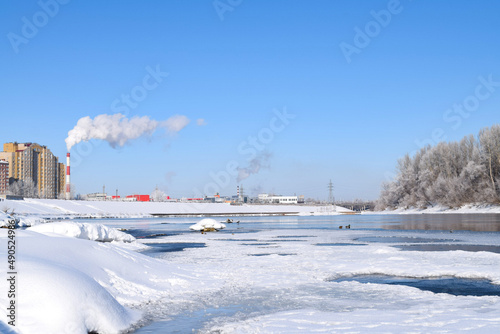 Winter cityscape with river, houses, factory pipes