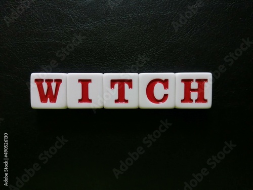 Photo The word Witch is spelled with white and red tiles on a black leather background