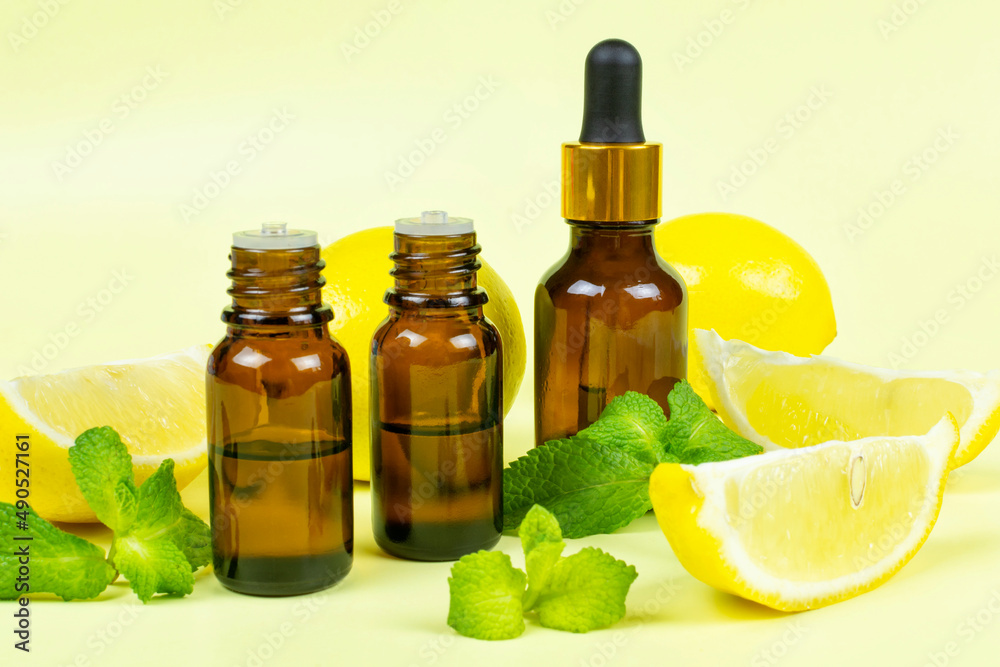Essential oil of fragrant lemon and peppermint (mint) in dark brown glass bottles with a yellow background. Aromatherapy (anti-fatigue, relaxation), spa, skin care. Essential oil of fragrant lemon and peppermint (mint) in dark brown glass bottles with a yellow background. Aromatherapy (anti-fatigue, relaxation), spa, skin care.