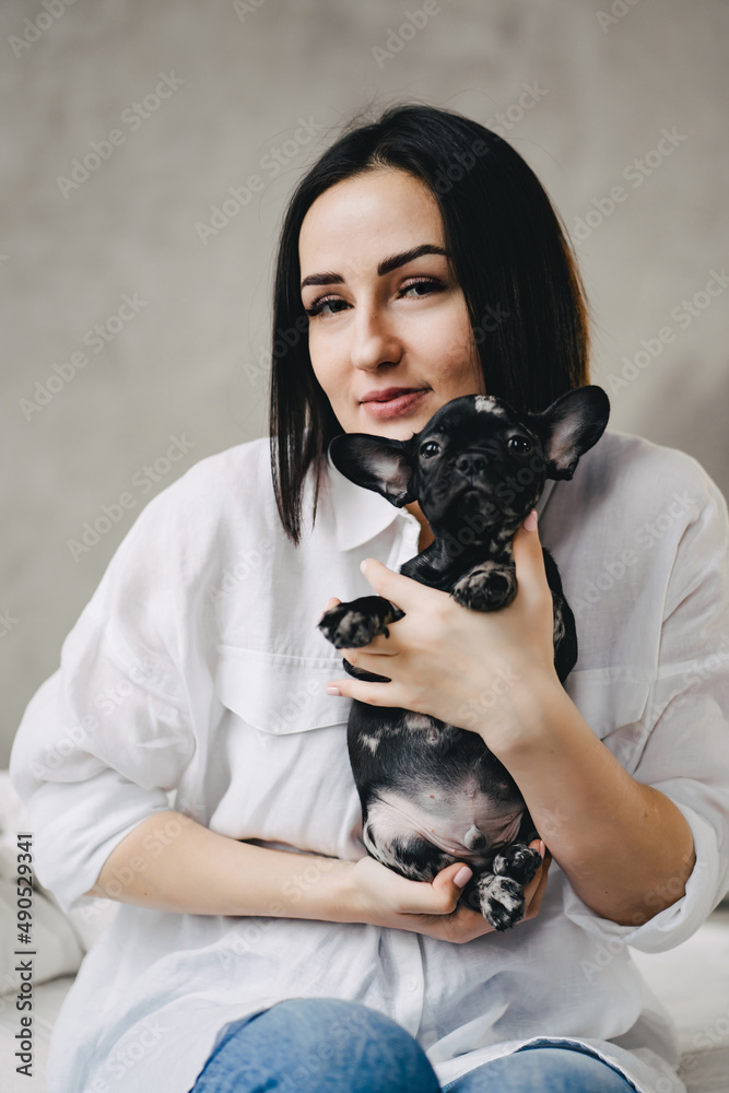 happy attractive brunette woman with a French Bulldog puppy in a bedroom.