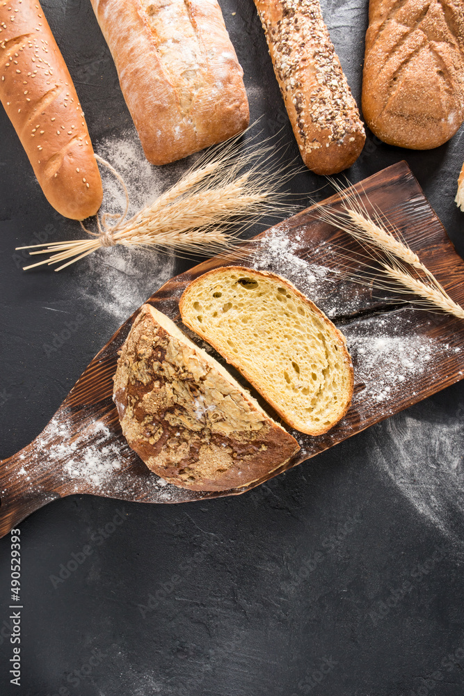 vertical flat view with a copy of the space on the assortment of freshly baked bread in the bakery. black background with scattered flour.
