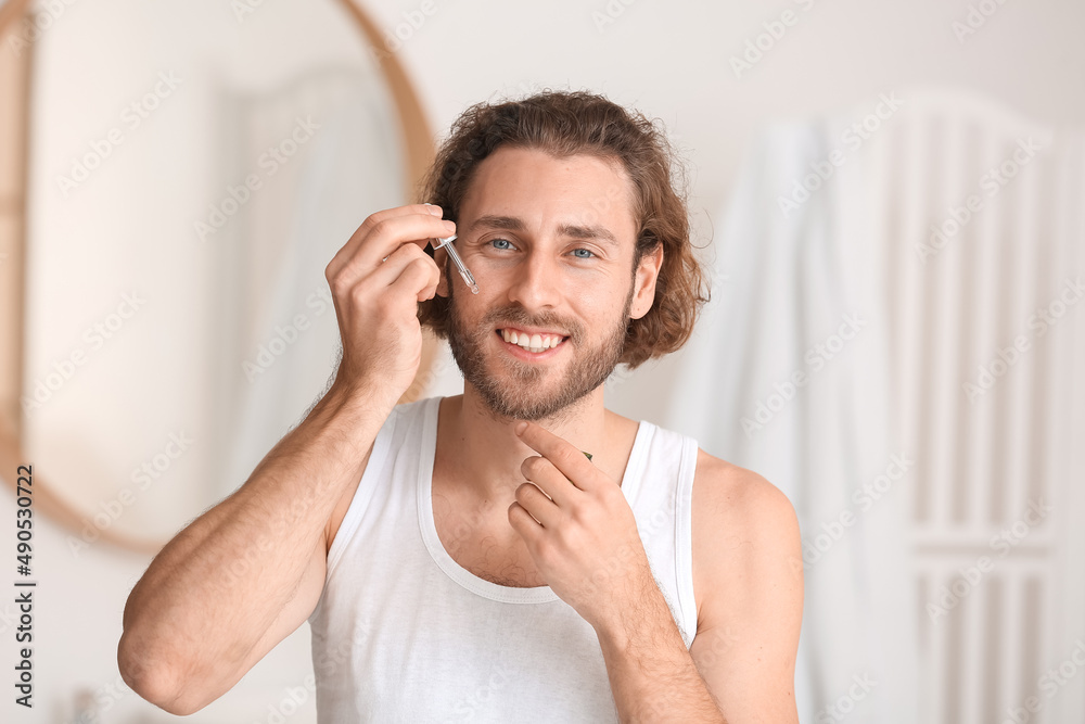 Young man using serum for skin care in bathroom Young man using serum for skin care in bathroom