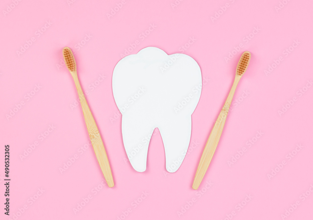 White tooth and wooden toothbrushes on a pink background. Dental care concept, banner, copy space