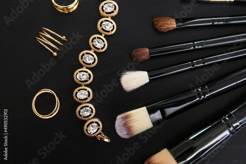 Composition with makeup brushes and different jewelry on dark background