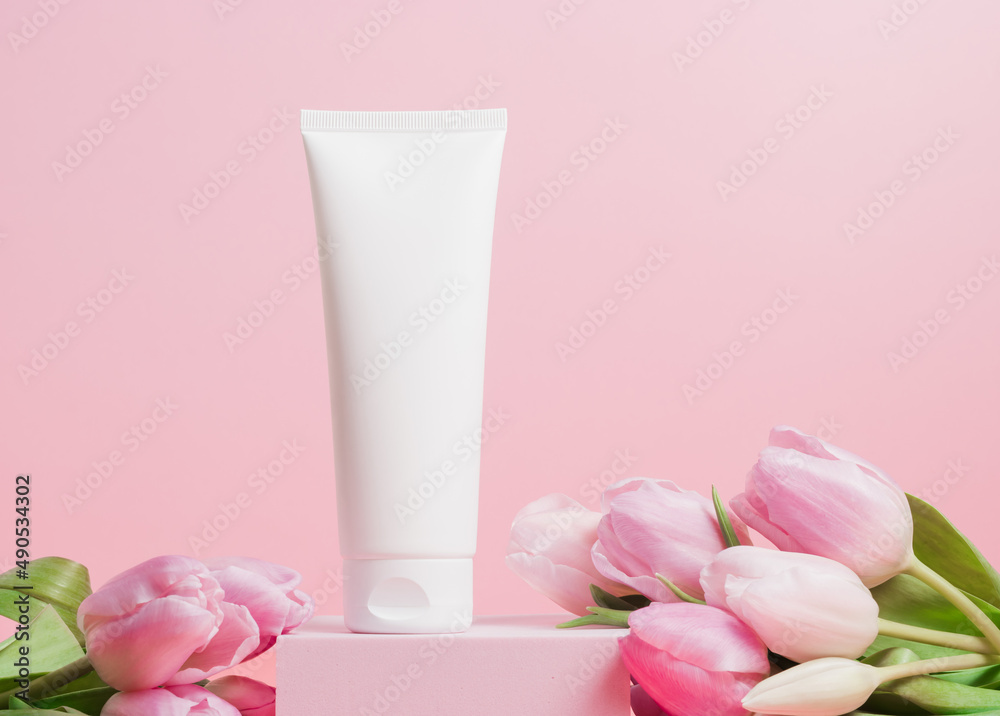 White unbranded mockup cosmetic tube of face cream or body lotion with tulip flowers on pink background, spring skin care cosmetics White unbranded mockup cosmetic tube of face cream or body lotion with tulip flowers on pink background, spring skin care cosmetics